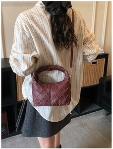 Gros plan d'un sac dumpling en cuir tressé bordeaux avec texture et bandoulière fine