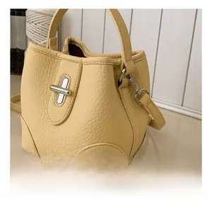 Close-up of light yellow bucket bag with silver metal swivel lock and leather handle