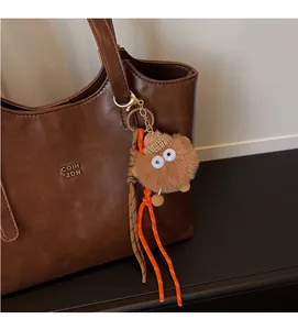 Pendentif monstre en peluche marron avec de grands yeux et bonnet sur un cabas