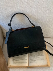 Minimalist black textured leather handbag with gold logo plaque on vintage book background