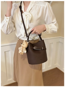 Detail of dark brown leather bucket bag with silver buckle and plush bear pendant