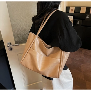 Dettaglio di una borsa tote grande in finta pelle marrone chiaro indossata a spalla
