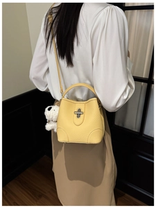 Detail of yellow pebbled leather bucket bag with silver twist lock and plush puppy charm