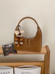 Caramel brown hobo handbag in matte leather with a stylish plush bead charm on wood shelf