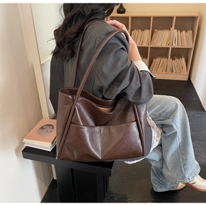 Dettaglio della borsa tote marrone scuro in pelle con tasca frontale indossata da una modella