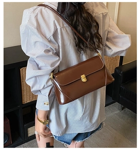 Brown faux leather baguette bag with gold metal clasp shown on shoulder with striped shirt