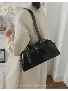 Close-up of black glossy leather Boston bag with adjustable shoulder straps and tag