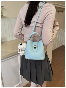 Detail of light blue textured leather bucket bag with silver lock and plush puppy charm