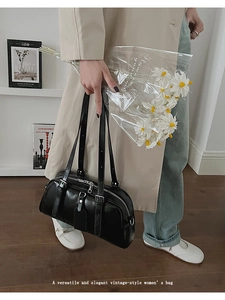 Close-up of a black leather Boston bag with silver zippers in a cozy indoor setting