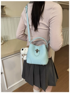 Close-up of light blue leather bucket bag with silver lock and plush puppy charm decor