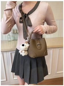 Detail of dark brown bucket bag with lychee texture, metal lock, and plush dog charm