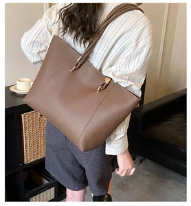 Detailed view of deep brown leather tote bag worn by model in a cozy indoor setting
