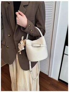 Detail of cream leather bucket bag with metal buckle and cute bunny charm accessory