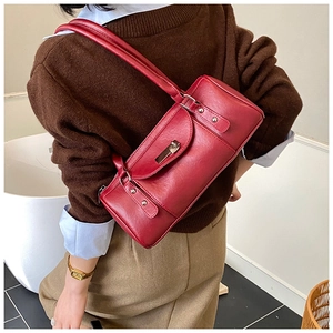 Close-up of a red cylindrical shoulder bag featuring a metallic swivel lock and rivets