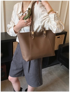 Detailed view of brown leather tote bag with gold hardware worn on model's shoulder