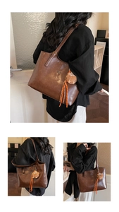 Détail d'un sac cabas marron foncé avec pendentif en peluche et accessoire à pampilles