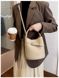 Litchi pattern cream bucket bag with silver buckle and adjustable shoulder strap worn by model