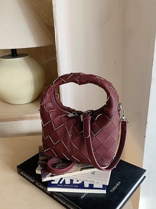 Sac bandoulière bordeaux tressé avec poignée supérieure sur des livres d'art épurés