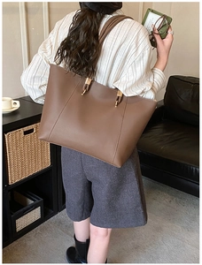 Detail of a large brown leather tote bag with gold metal rings and vertical stitching