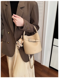 Beige pebble leather bucket bag with metal buckle and plush bear charm on model