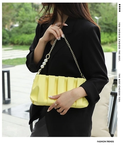 Detailed view of yellow ruched baguette bag with gold chain and pearl accents