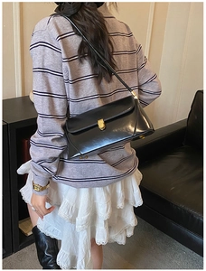 Detail of black leather baguette bag featuring a gold clasp and smooth polished texture