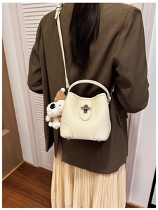 Detail of creamy litchi grain bucket bag with metallic twist lock and plush puppy charm