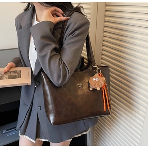 Detail of dark brown tote bag with metal logo, plush charm, and striped silk ribbon