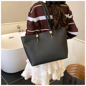 Detail view of large black tote bag with gold hardware shown on a female model
