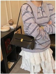 Close-up of black leather rectangular shoulder bag with elegant gold metal push-lock