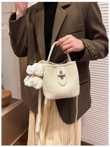 Close-up of cream bucket bag with lychee texture leather and plush puppy pendant