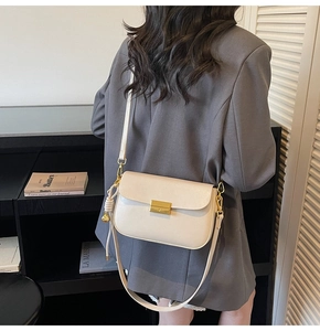 Detail of a beige leather crossbody bag with gold buckle and fringe on a model
