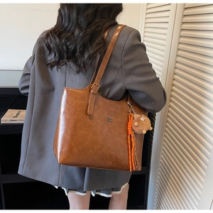 Brown vintage faux leather tote bag with charm pendant worn over shoulder on a grey blazer