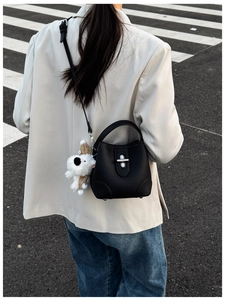 Detail of black pebbled leather bucket bag with silver clasp and plush puppy charm