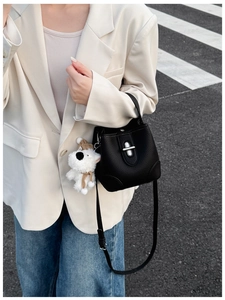 Detail of black lychee grain bucket bag with silver clasp and plush dog charm