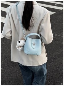 Close-up of light blue leather bucket bag with cute plush puppy charm on handle