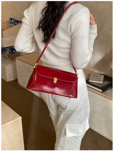 Detail of glossy red underarm bag with gold metal buckle worn with a white knit top