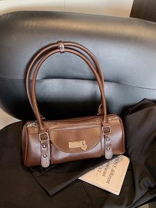 Brown faux leather cylinder Boston bag with top handles and a heart pendant on a leather chair