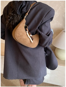 Close-up of brown hobo bag with vintage beaded charm on a shoulder in minimalist interior