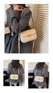 Detail of cream shoulder bag with golden metallic lock and side knot on a gray blazer