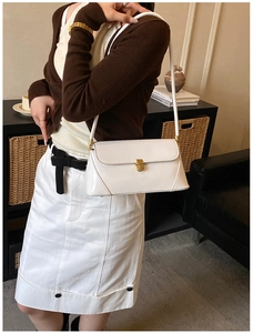 Detail of white leather baguette bag with gold buckle worn by model on shoulder