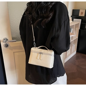 Détail d'un sac boîte beige avec gaufrage autruche, zips argentés et poignée haute