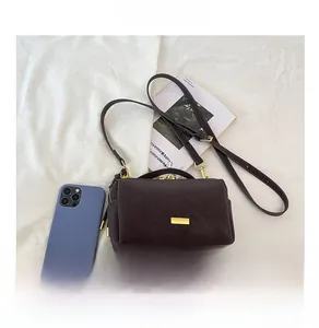 Chocolate brown leather boston bag with gold hardware shown next to a smartphone for scale
