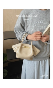 Modische cremeweiße Lederhandtasche mit plissierten Seiten und Schloss am Modell gezeigt