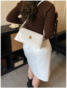 Side view of white baguette shoulder bag with gold clasp worn by a model
