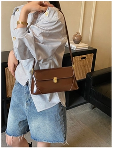Detail of a dark brown glossy baguette bag with a gold rectangular metal buckle