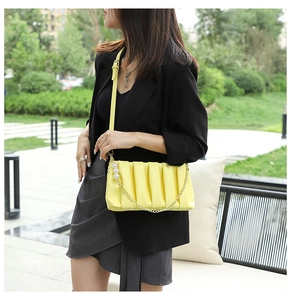 Detail of yellow pleated shoulder bag with gold chain and pearls on a female model
