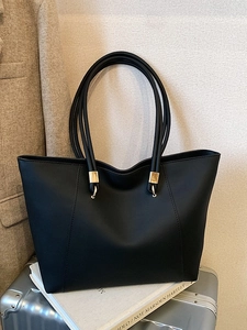 Minimalist black leather tote bag with gold metal accents on a silver suitcase for travel