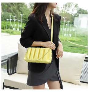 Detail of yellow pleated crossbody bag featuring golden chain and pearl ring charm