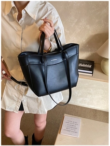 Close-up of minimal black leather tote bag with white logo and dual handle structure